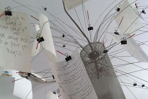 Poetry hand-written on pages suspended w/ binder clips on a display